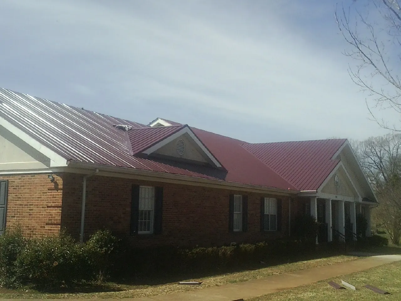 Red metal roof with gabled entries on a long brick building, from a Hail Damage Roof Repair job in Wilmette