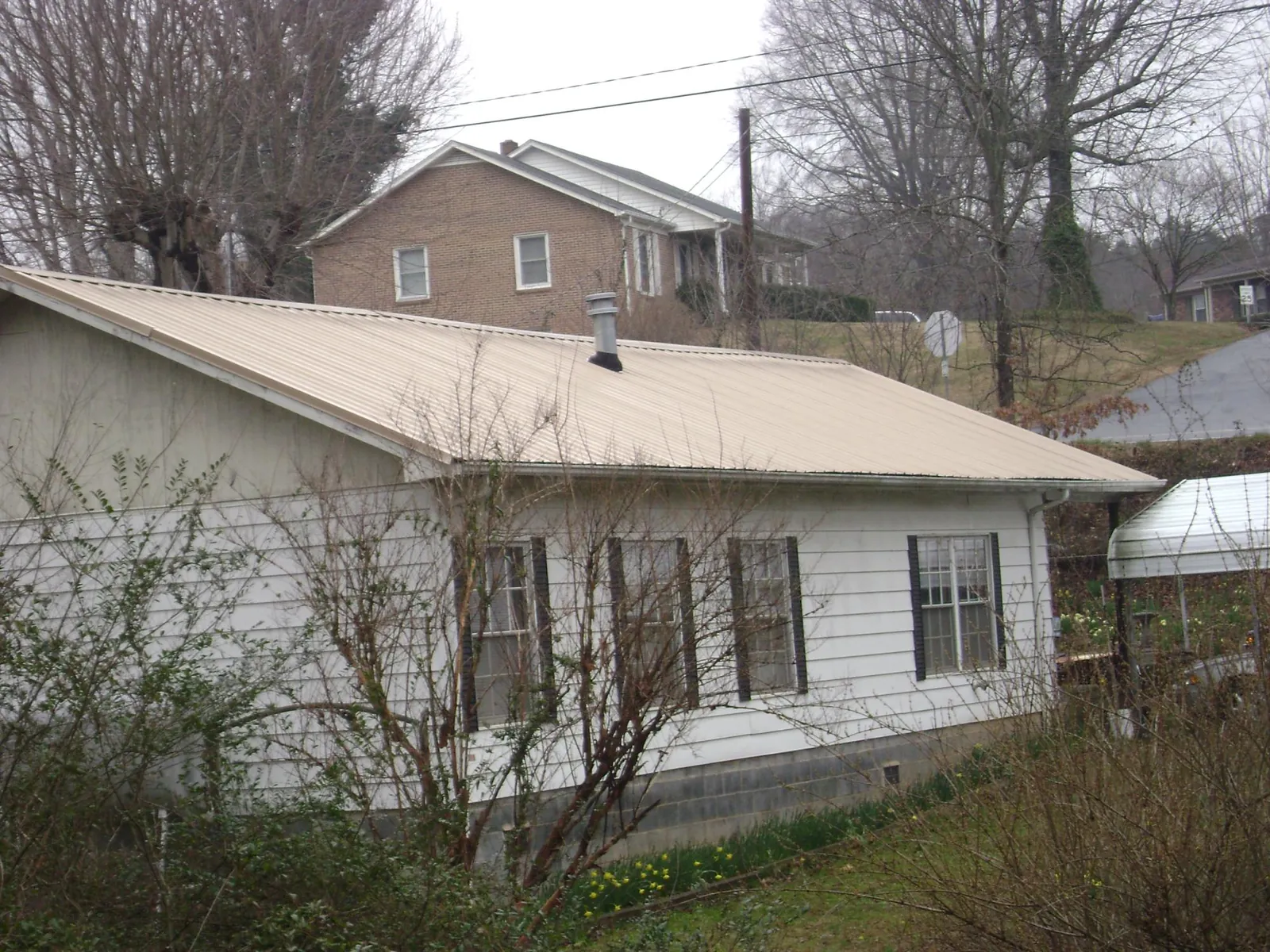 Tan metal roof on a white sided house set into a hillside — Commercial Roofing by Roofing Brothers in Wilmette